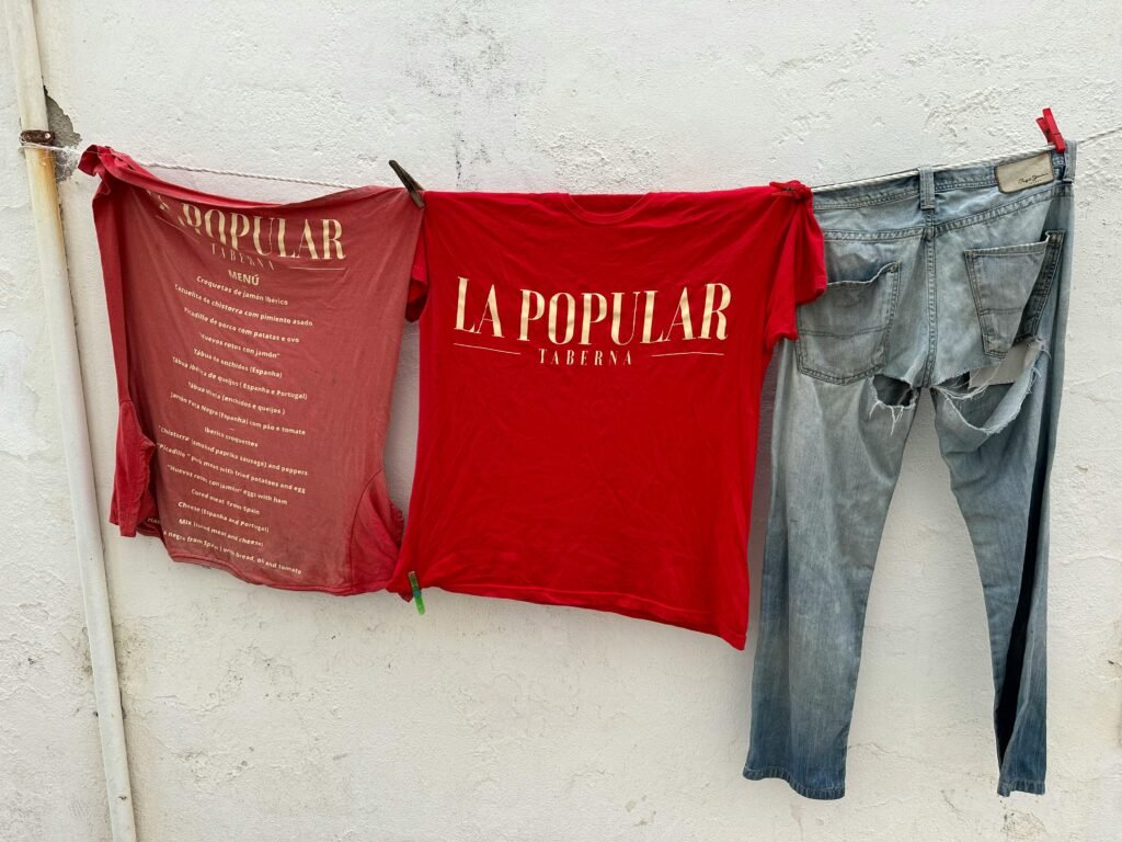 Red T-shirts and jeans drying on a clothesline against a white wall in Ericeira, Portugal.