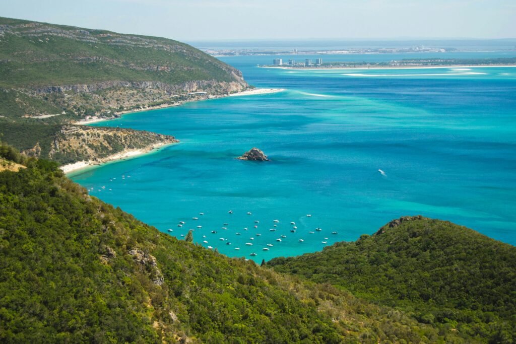 Breathtaking aerial view of Setúbal coastline with turquoise waters and lush green hills.